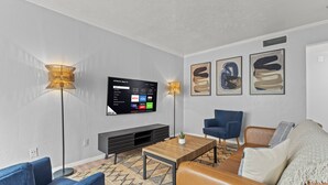 A modern living room with a flat-screen TV, two floor lamps, a coffee table, a sofa, and a TV stand. - Stylish & Comfy | King Bed | Near Love Field | DT (Dallas)