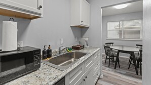 A kitchen with a microwave, sink, and cabinets. There is a dining table with chairs in the background. - Stylish & Comfy | King Bed | Near Love Field | DT (Dallas)