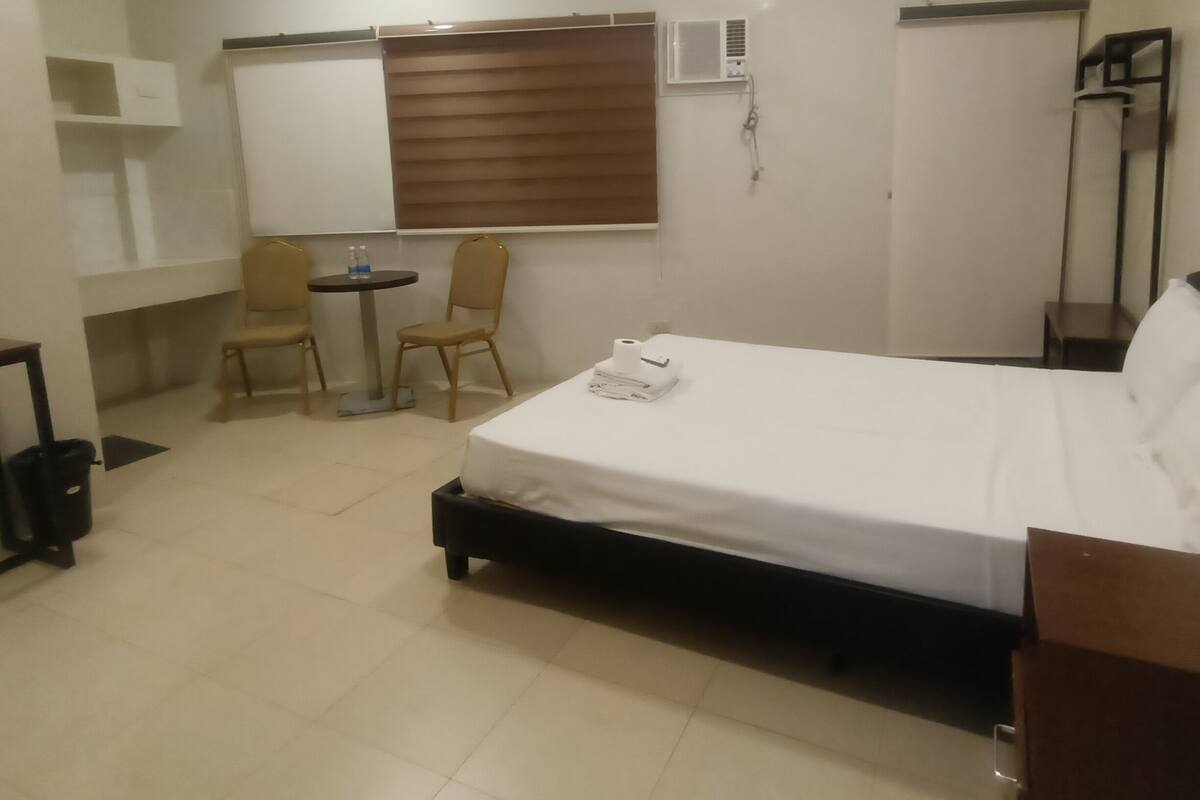 A hotel room with a bed, a chair, a small table, and a whiteboard.