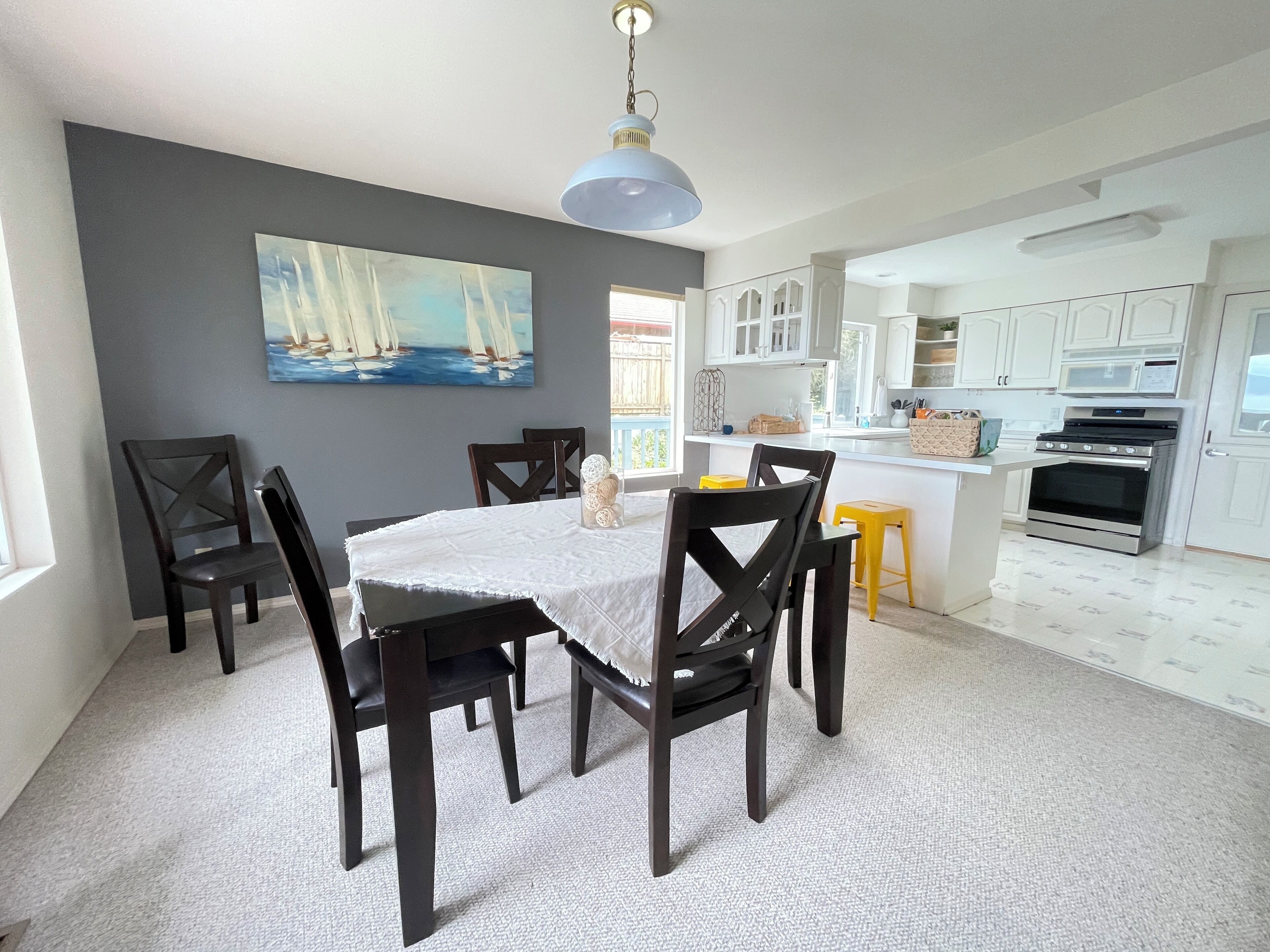 Een eetruimte met een tafel, stoelen, een schilderij aan de muur en een keuken op de achtergrond.