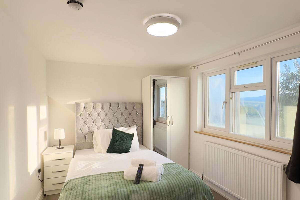 A bedroom with a bed, a nightstand, a radiator, and a window with a view.