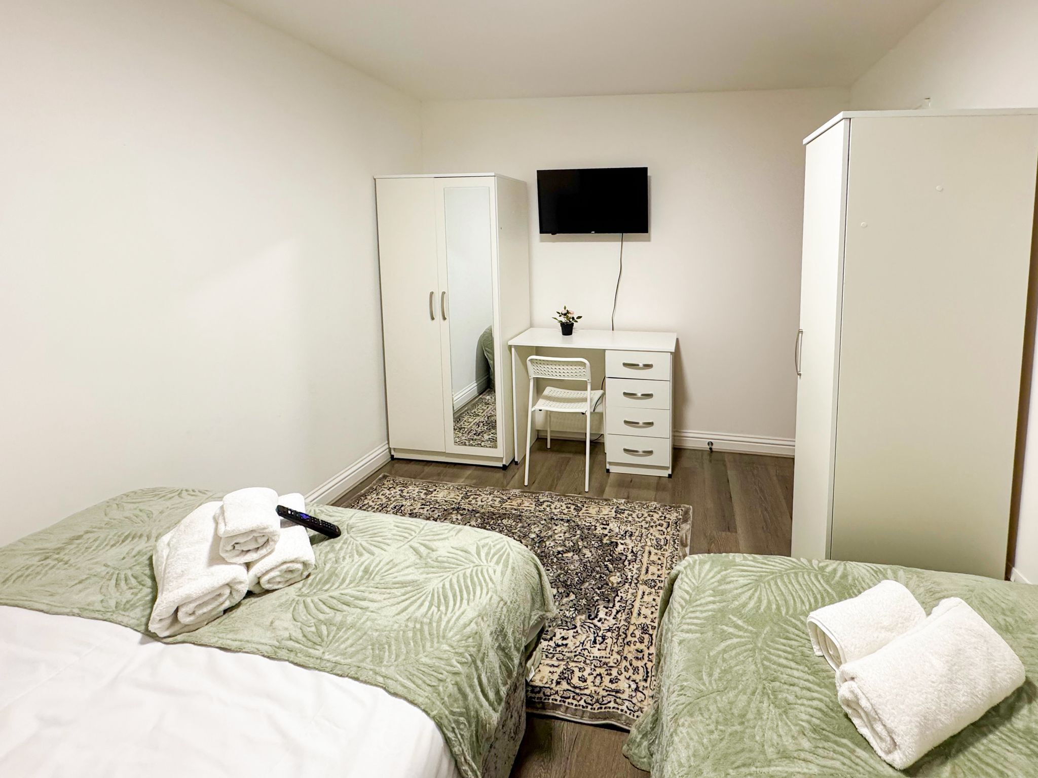 A bedroom with two beds, a desk, a chair, a wardrobe, and a TV.