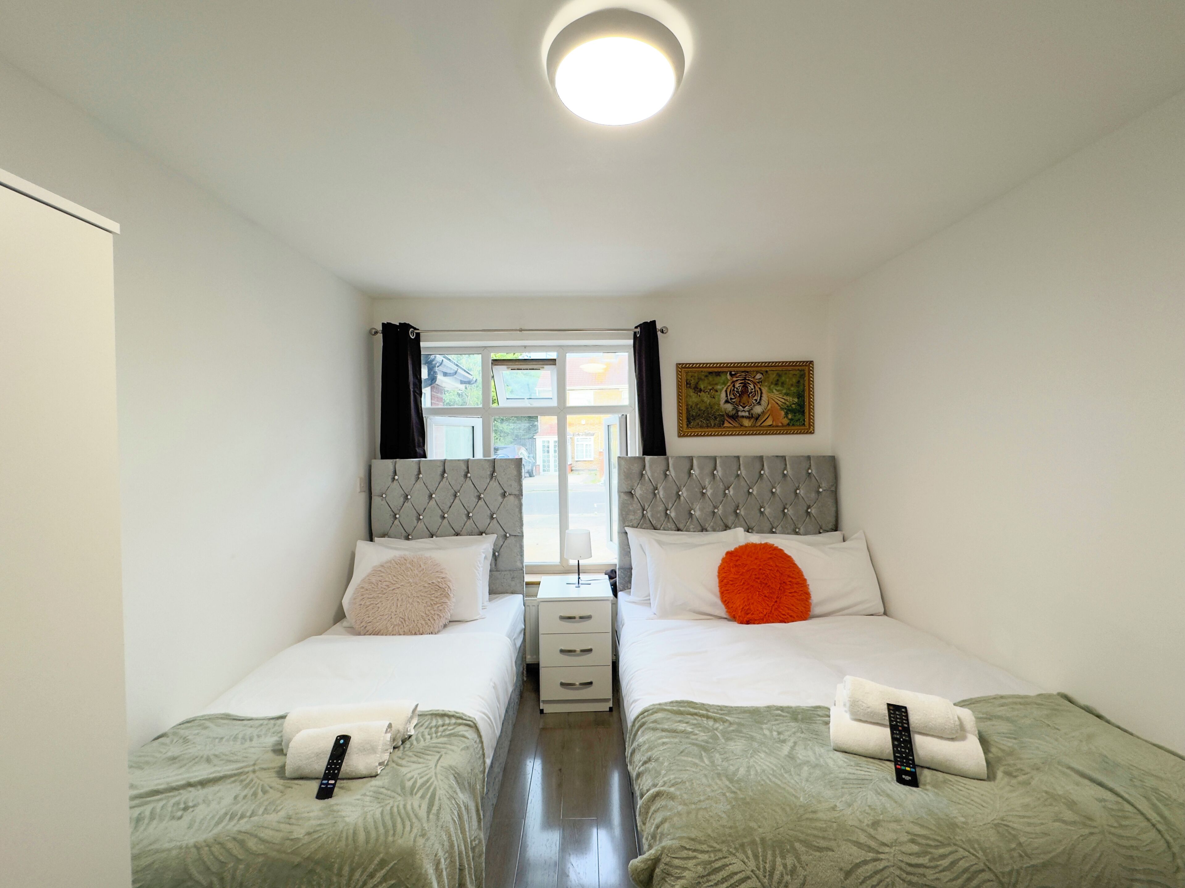 Una camera d'albergo con due letti, ognuno con una testata imbottita, un'ampia finestra con tende, un quadro appeso alla parete e un telecomando su ogni letto.