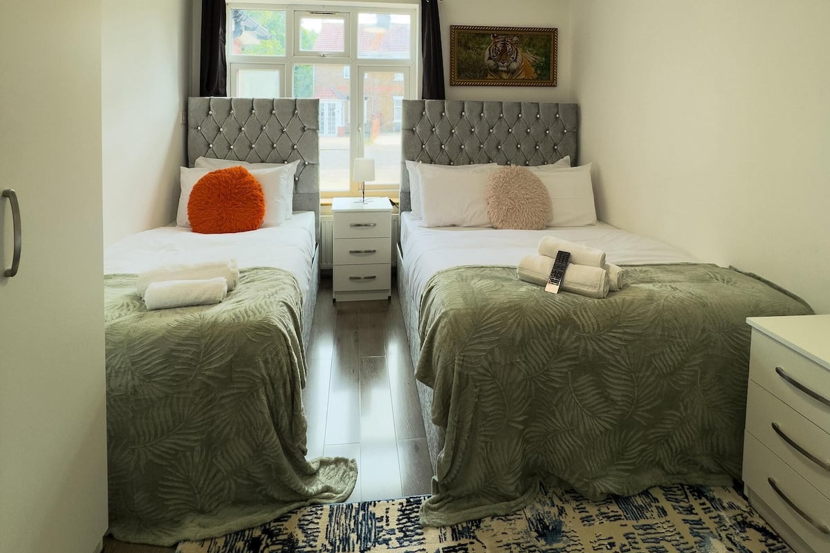 A hotel room with two beds, a window, a painting, and a patterned rug.