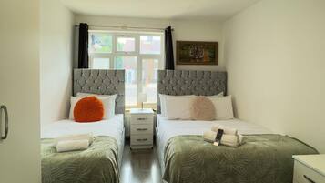 A hotel room with two beds, a window, a painting, and a patterned rug.