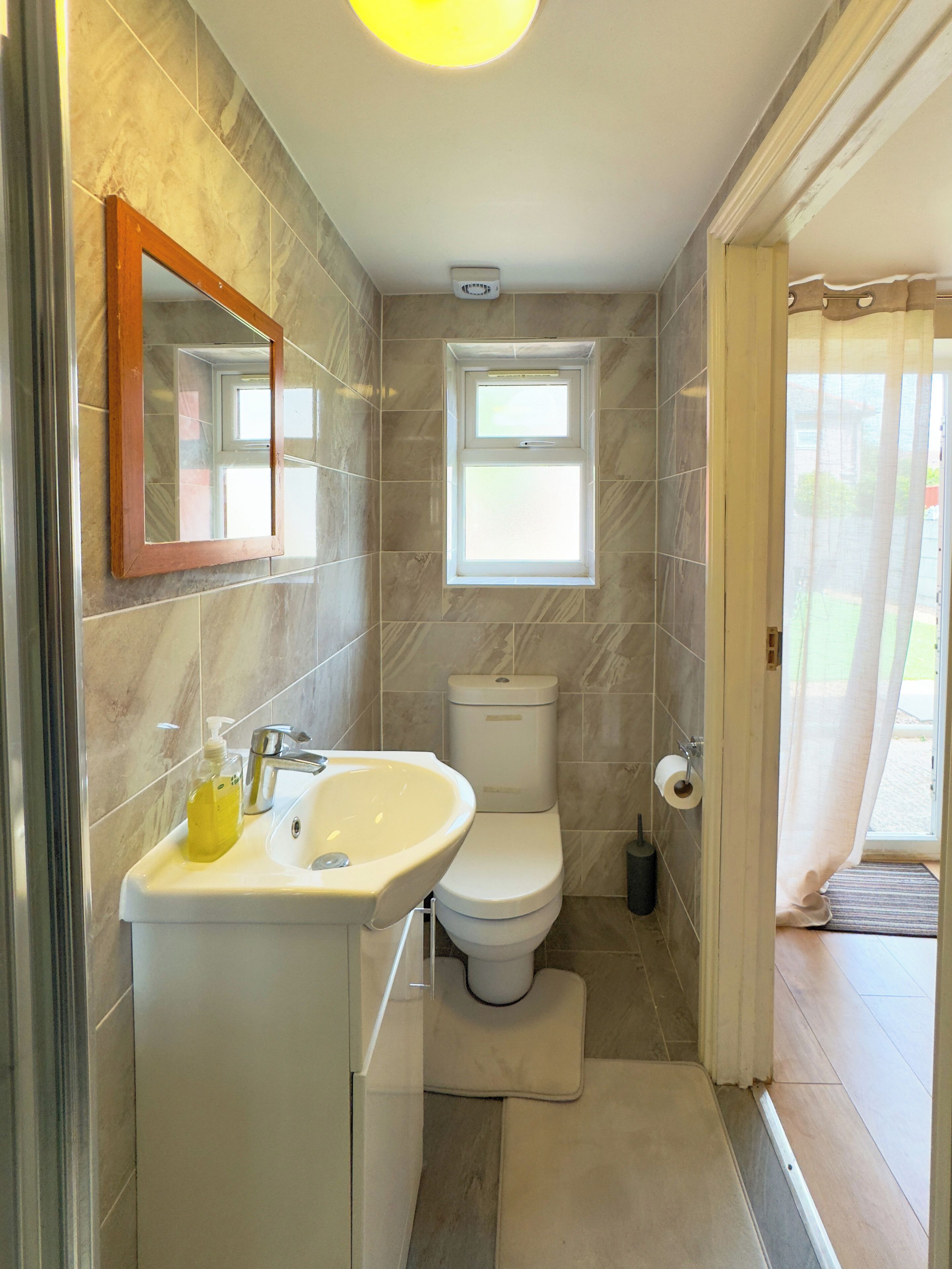 A bathroom with a sink, mirror, toilet, and a window.