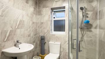 A modern bathroom with a glass-enclosed shower, a pedestal sink, and a toilet.
