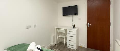 A hotel room with a bed, a desk, a television, and a door.