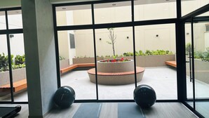 A modern indoor space with large windows, a central planter with flowers, and exercise equipment. - Nephi’s Villas Modern 2 Bedroom Apartment with Pool, Gym. Miraflores Location (Miraflores)