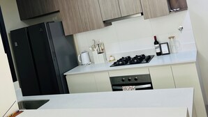 A modern kitchen with wooden cabinets, a black refrigerator, a stove, and a white countertop. - Nephi’s Villas Modern 2 Bedroom Apartment with Pool, Gym. Miraflores Location (Miraflores)