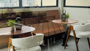 A modern dining area with a round table and white chairs, large windows with a city view, and potted plants on the windowsill. - Nephi’s Villas Modern 2 Bedroom Apartment with Pool, Gym. Miraflores Location (Miraflores)