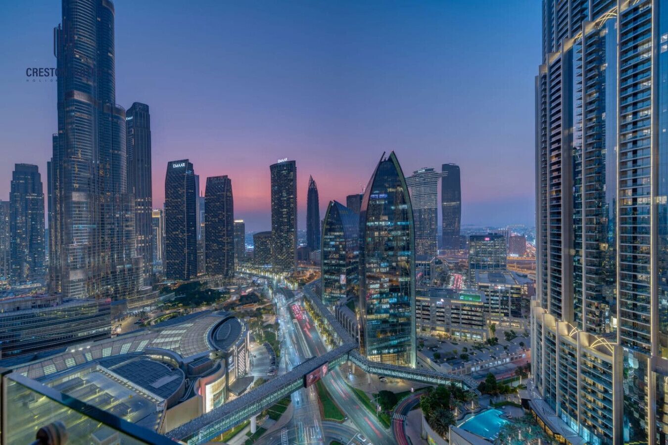 A cityscape with modern skyscrapers, a prominent curved building, and a well-lit highway.