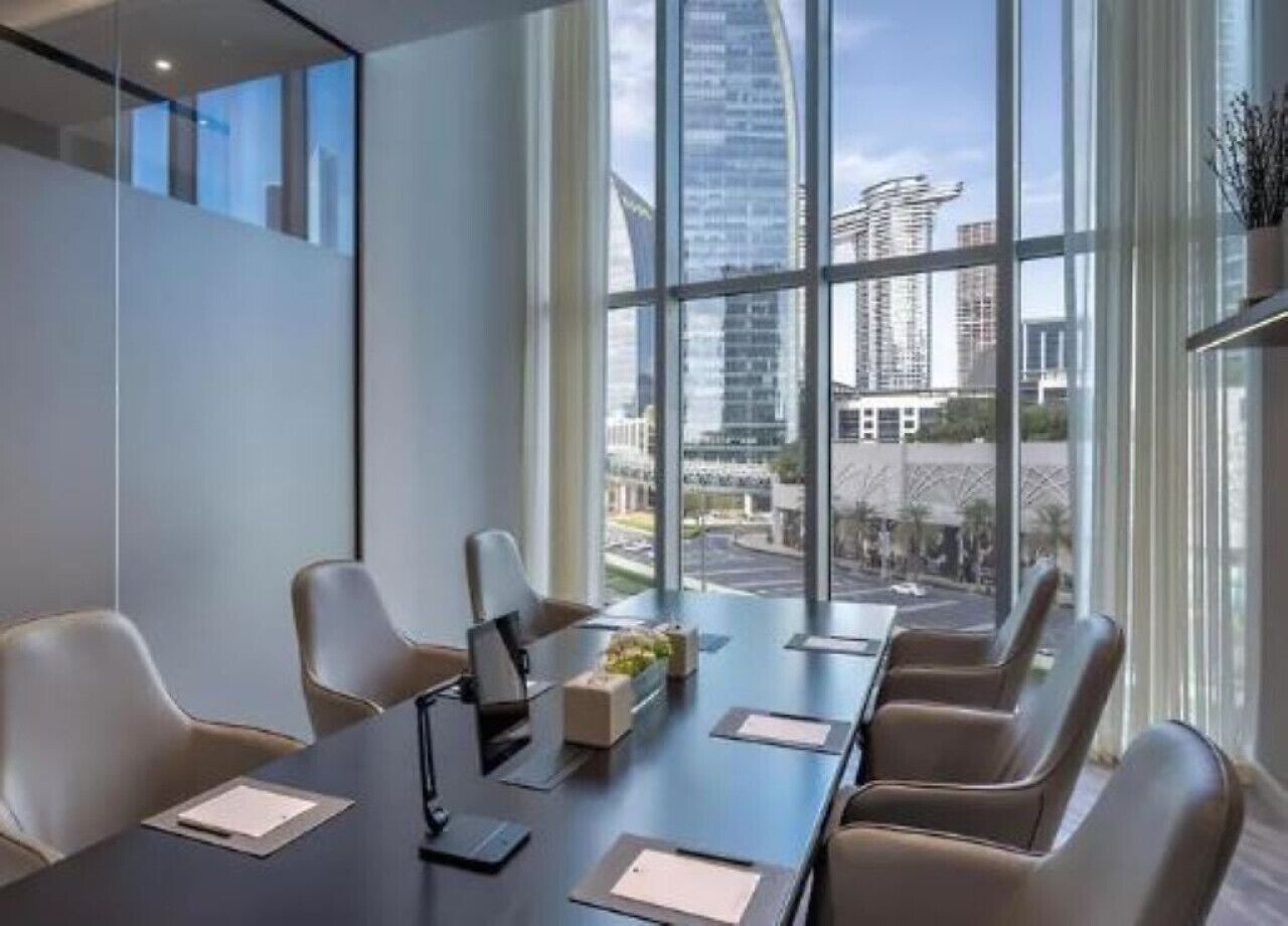 Una sala conferenze moderna con un lungo tavolo, sei sedie e ampie finestre che si affacciano su alti palazzi.