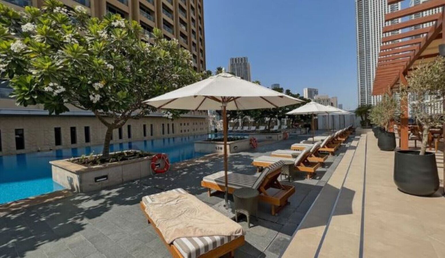 Un espace piscine aménagé sur le toit, avec des chaises longues et des parasols, entouré de grands immeubles.