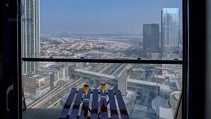 A high-rise hotel room with a panoramic city view, a small table with two glasses, and a window overlooking a busy urban area. - Chic Studio w/ Stunning City View + Pool Access (Dubai)