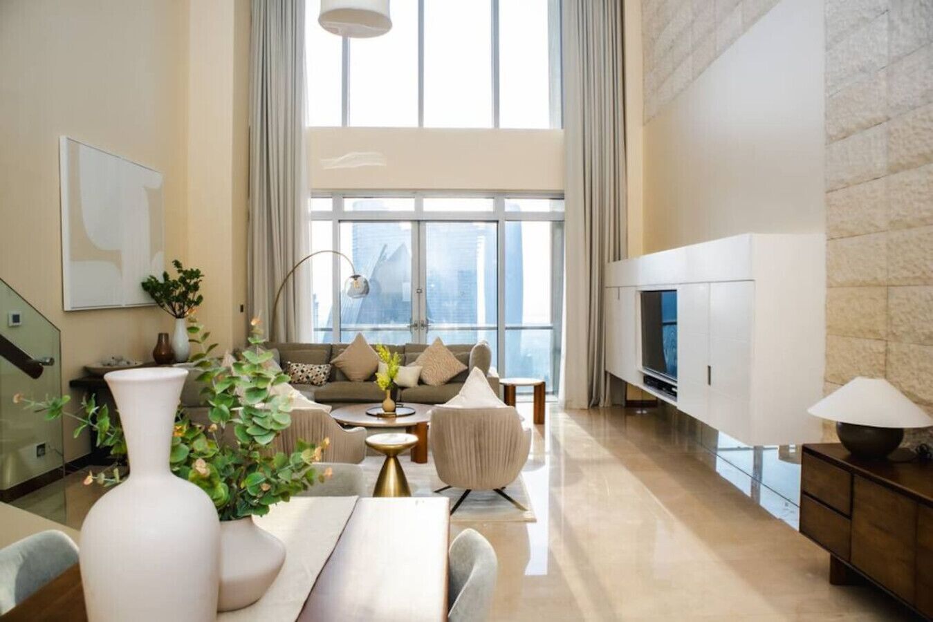 A spacious living room with a large window, a sofa set, a TV, and a dining area.