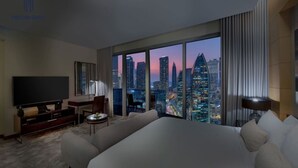 A hotel room with a large bed, a TV, a desk, and a view of a cityscape at dusk. - Skyline Studio | Burj Views, Mall & Pool Bliss (Dubai)