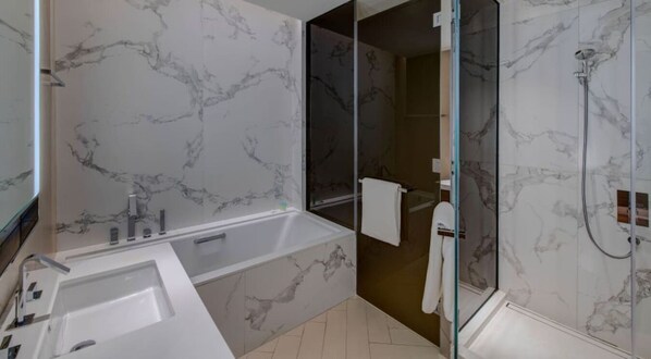 Un baño moderno con salpicadero de mármol, una bañera grande, una ducha con mampara de vidrio y un lavamanos blanco.
