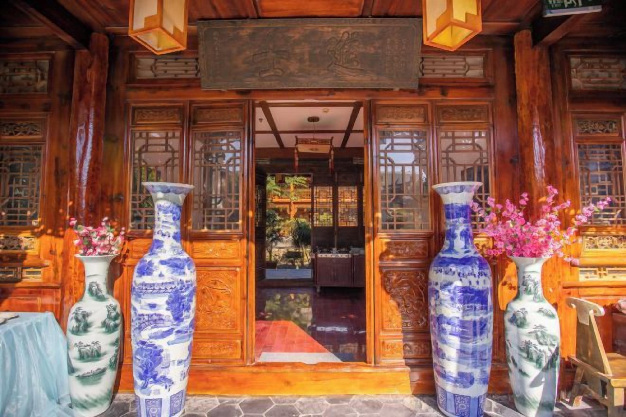 A traditional wooden building entrance with large vases and a red mat.