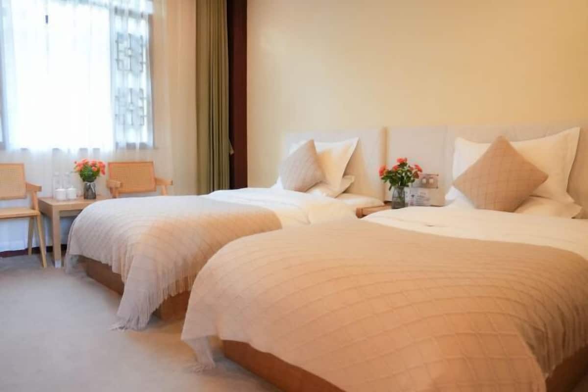 Una habitación de hotel con dos camas, una mesita con un florero y una silla.