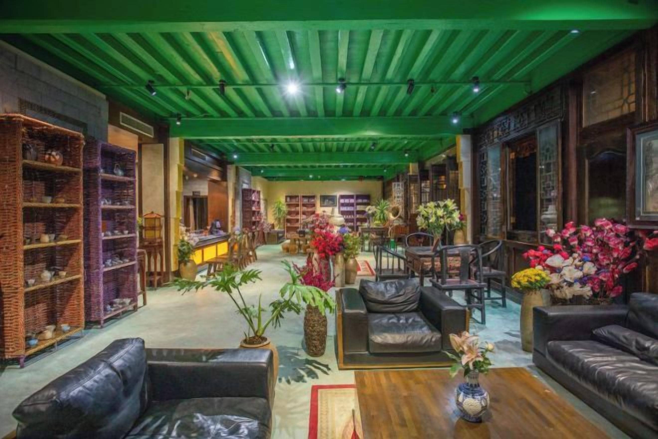 A spacious interior with a green ceiling, leather sofas, wooden tables, and a variety of plants.