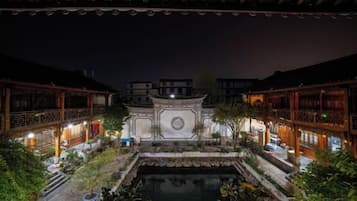 A courtyard with traditional architecture, a central fountain, and surrounding buildings with illuminated windows.