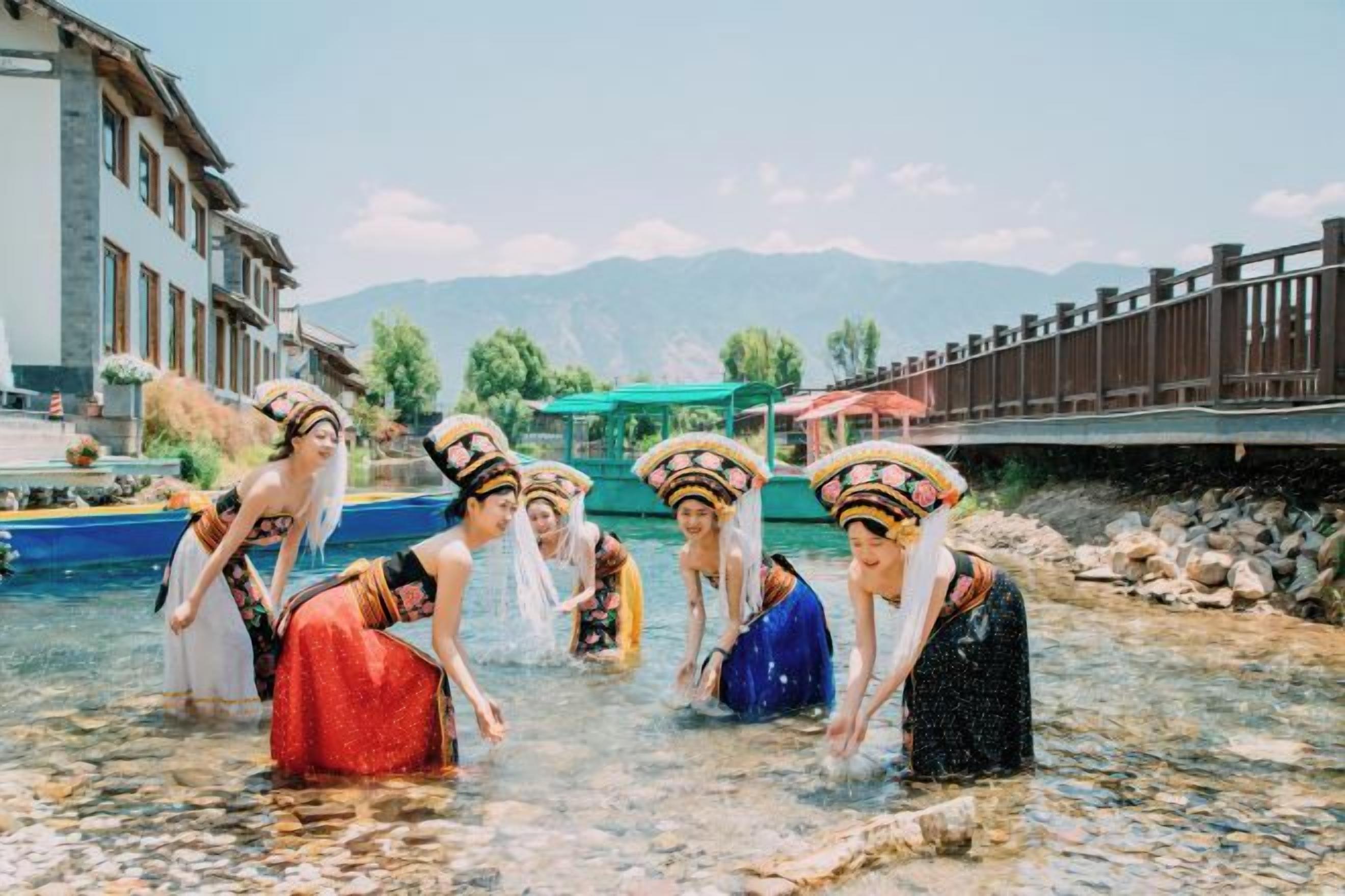 A group of people in traditional attire standing in a shallow water body, with buildings and a bridge in the background.