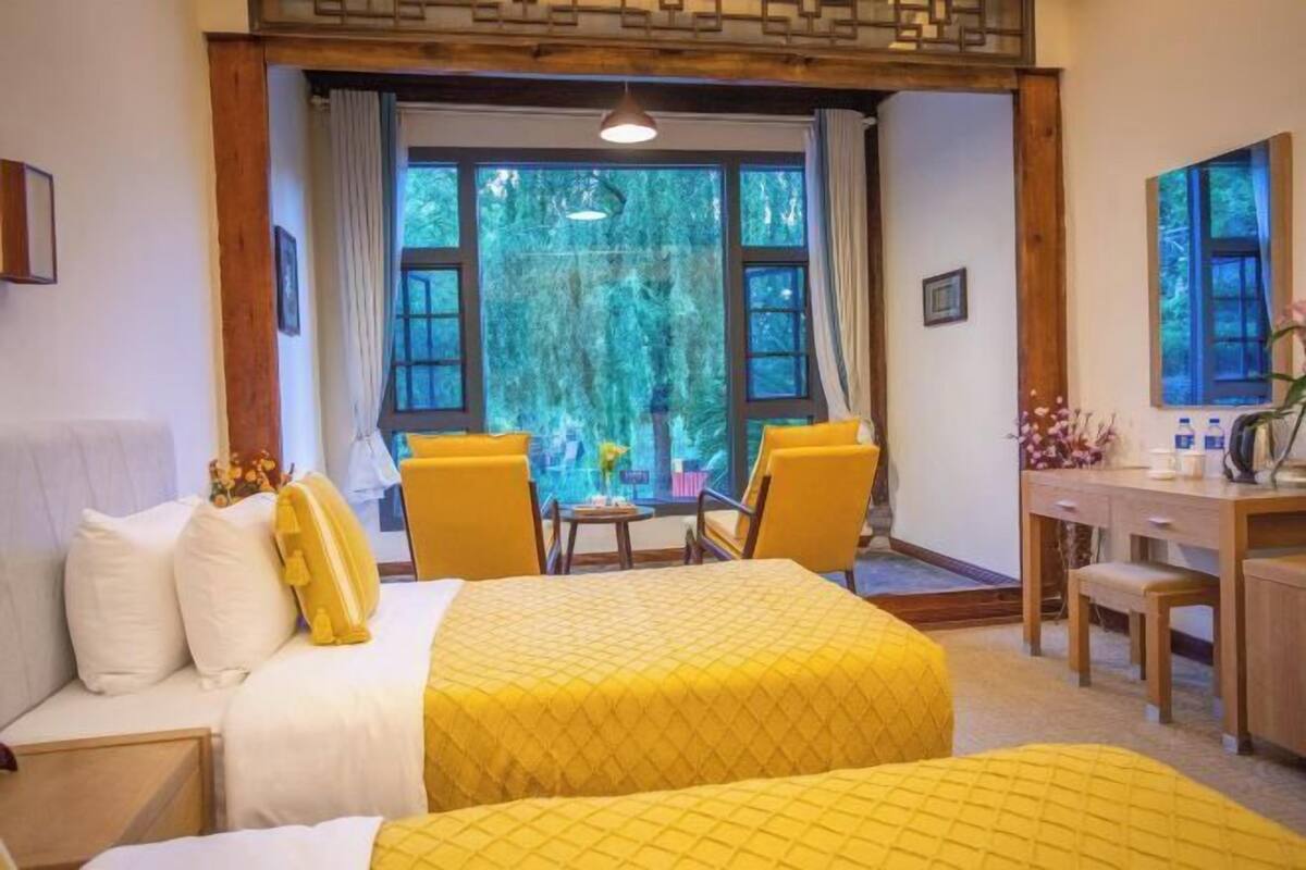 Una habitación con dos camas, un escritorio y una ventana con vista a árboles.