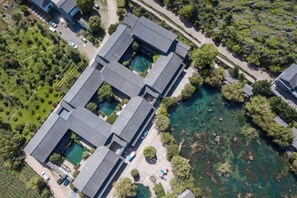 Luchtbeeld van een gebouw met verschillende rechthoekige constructies, omringd door groen en een waterpartij.