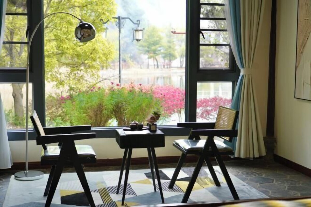 A room with a large window, a desk, two chairs, and a lamp.