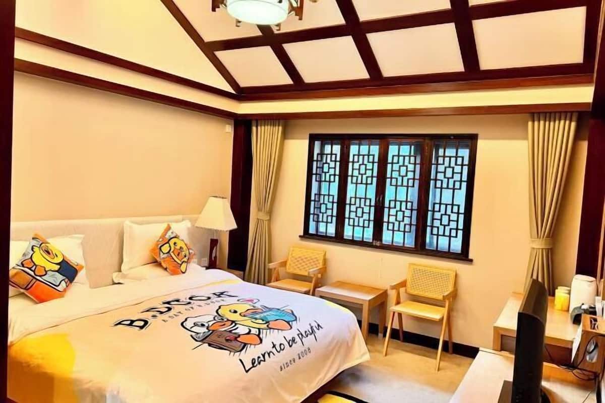 Habitación de hotel con cama, escritorio, silla, televisor y ventana con cortinas.