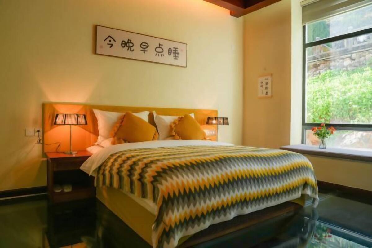 Un dormitorio con cama, lámparas de noche, ventana con vistas y una obra de arte colgada en la pared.