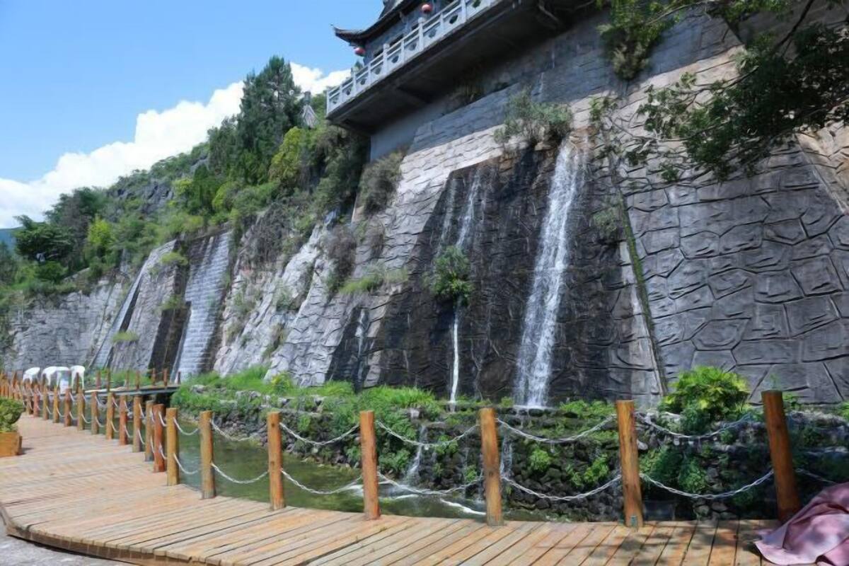 Un pasarela de madera que lleva a una construcción tradicional con pared de piedra y una cascada.