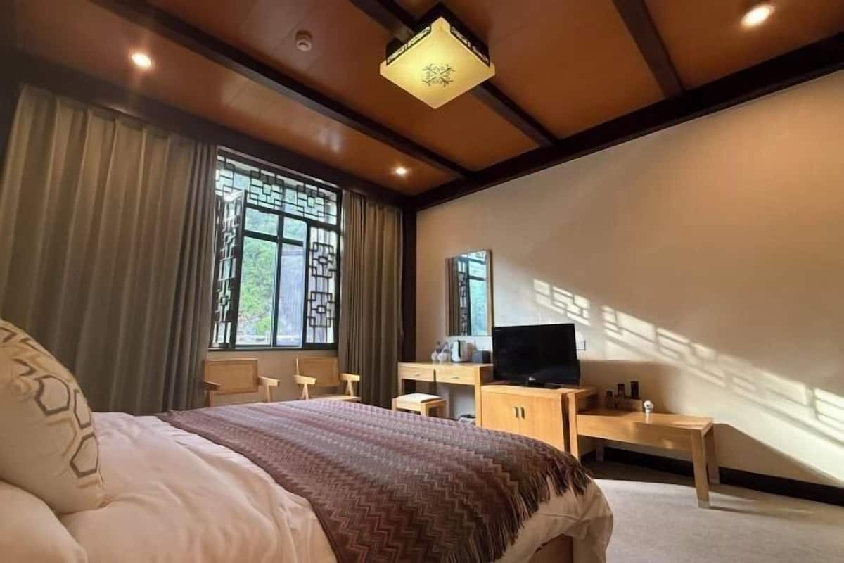 Un dormitorio con una cama, un escritorio, un televisor y una ventana con cortinas.