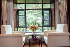 A room with two white chairs, a small table with a vase of flowers, and a large window with curtains. - Heqing Cunshi Manor · YouRan Residence (Heqing)