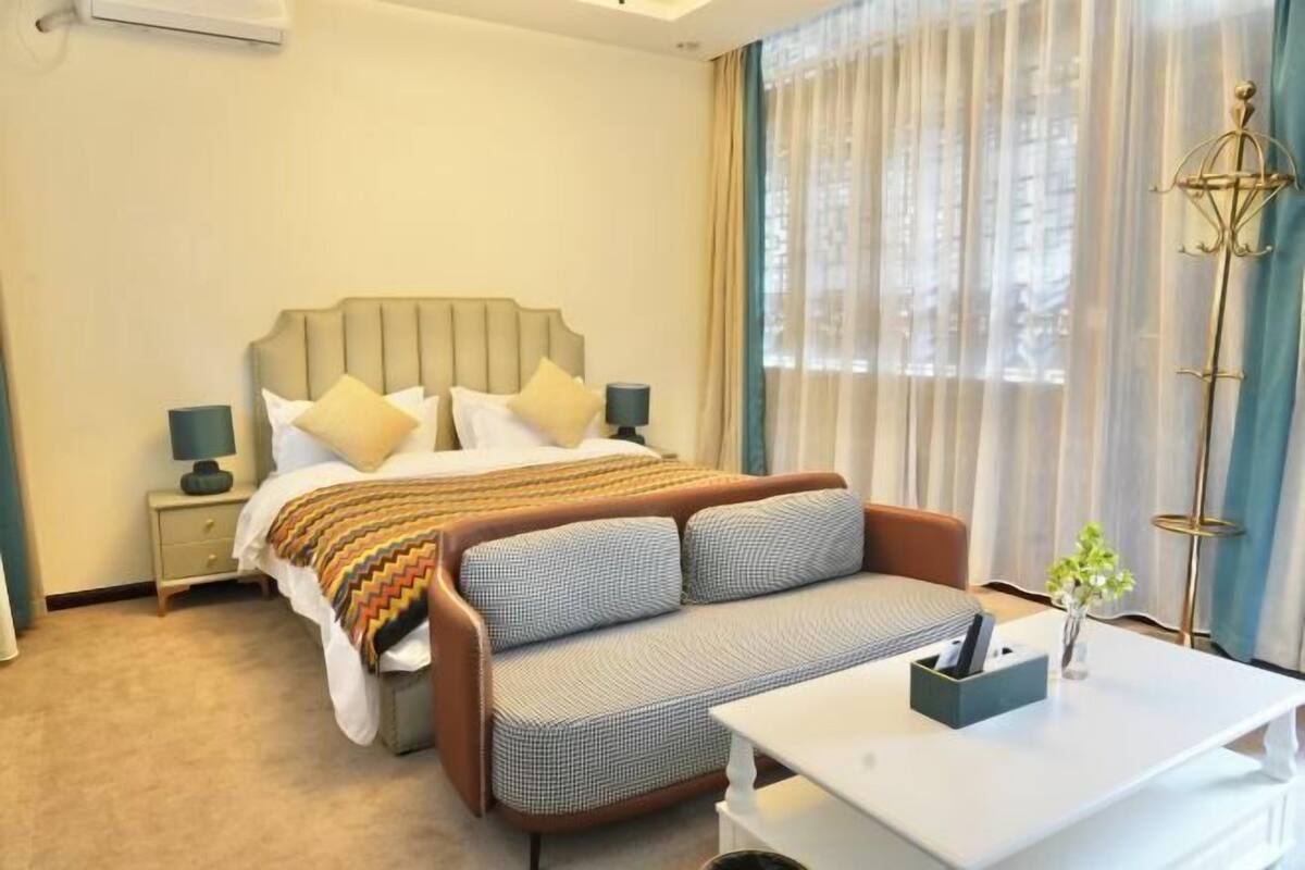 Habitación de hotel con cama, mesita de noche, lámpara, sofá y escritorio con un jarrón de flores.
