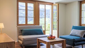 Une pièce chaleureuse avec un canapé, un fauteuil bleu et une table en bois sur laquelle sont disposés des fruits.
