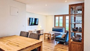 Un salon moderne avec une table à manger en bois, un canapé et un téléviseur fixé au mur.