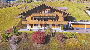 Un chalet à deux étages, doté d’un toit en pente, situé sur une colline avec une vue sur les montagnes.