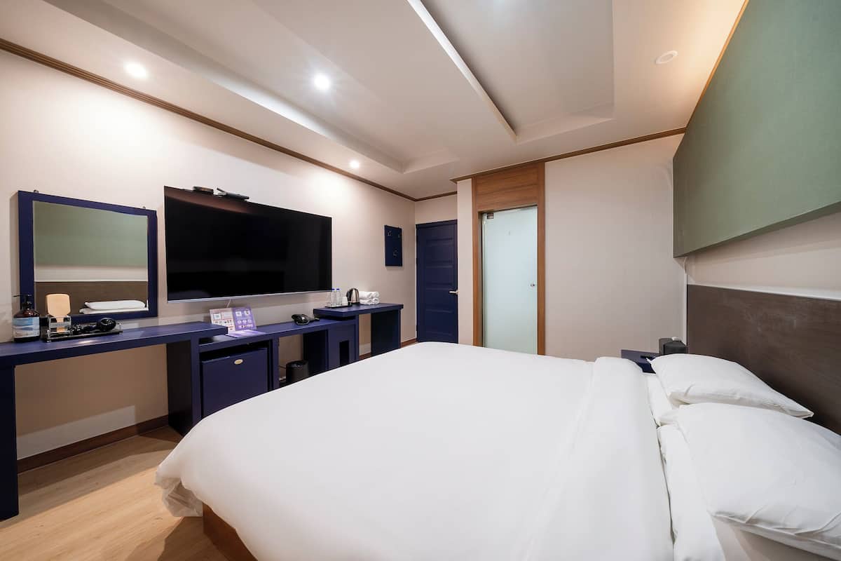 A modern hotel room with a large bed, a desk with a flat-screen TV, a mirror, and a small cabinet.
