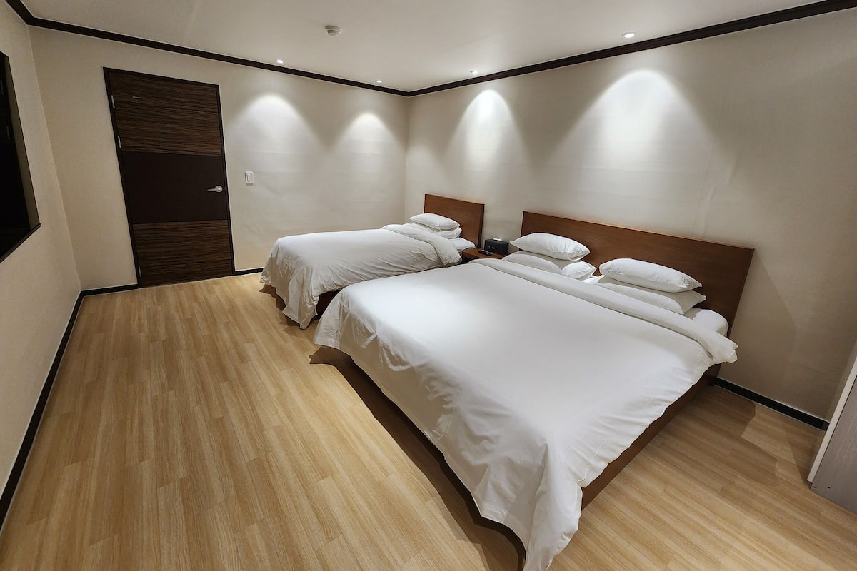A hotel room with two beds, wooden flooring, and a modern design.