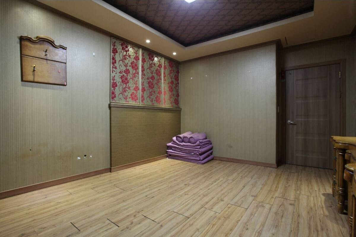 A room with wooden flooring, a stack of purple blankets, a wooden cabinet, and a door.