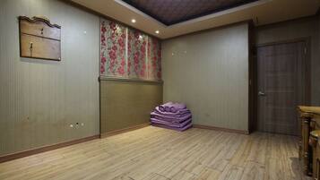 Habitación con suelo de madera, una pila de mantas moradas, un armario de madera y una puerta.