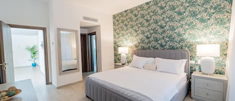 A hotel room with a large bed, two bedside tables with lamps, a ceiling fan, a patterned wallpaper, and a potted plant.