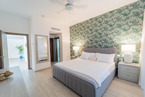Una camera d'albergo con un letto grande, due comodini con lampade, una ventola a soffitto, carta da parati decorata e una pianta in vaso.