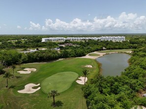 A golf course with bunkers, a pond, and a hotel in the background.