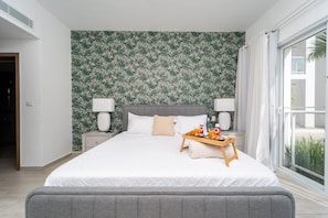 Quarto de hotel com uma cama grande, duas mesas de cabeceira, uma janela com cortinas e vista para o verde lá fora.