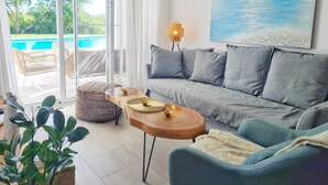 Una sala de estar moderna con un sofá gris, una mesa de centro de madera y vista a una piscina a través de puertas de vidrio amplias.