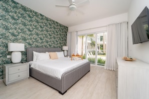 Quarto com cama, mesas de cabeceira, ventoinha no teto, TV e vista para o exterior.