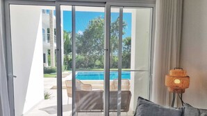 Habitación con puerta de vidrio corrediza que da a una zona de piscina, mobiliario de mimbre y una lámpara de pie.